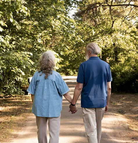An elderly couple walking together outdoors in a park, representing improved mobility and recovery after a Genicular Artery Embolization procedure.