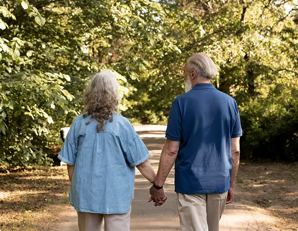 An older couple holding hands while walking through a park, illustrating the restored mobility and active lifestyle patients achieve after joint pain treatment.
